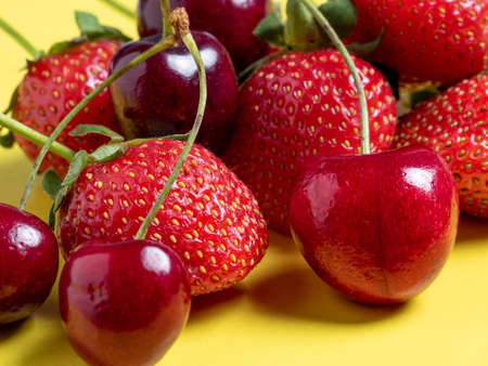Fresh juicy cherries and strawberries on a bright yellow background. Healthy food, vegetarianism,...