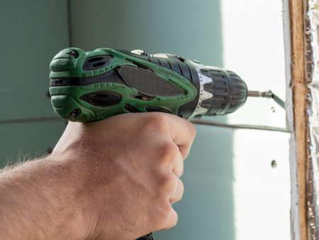 a man is holding a screwdriver and twisting the screw into the drywall. selective focus