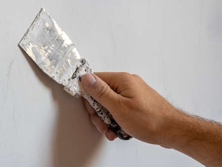 the hand of a worker with a spatula that works on the wall. Interior work, construction concept