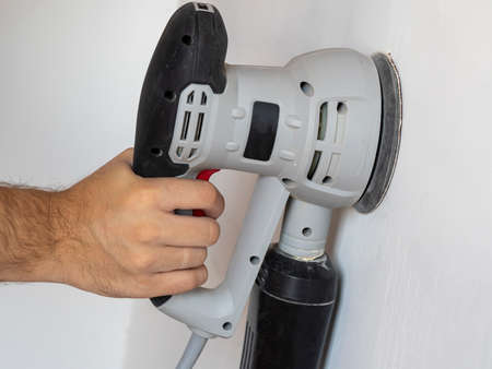 a Builder uses a sander to process a white concrete wall. Construction concertの写真素材