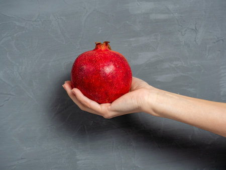 a woman's hand holds a ripe juicy whole pomegranate fruit on a gray background. Healthy and delicious fruit.の写真素材