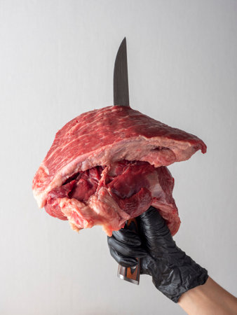 a piece of raw beef impaled on a knife in the hand isolated on a white background. Copy space, front...