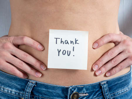 a paper sticker with the signature Thank you is pasted on the bare female stomach. The concept of...