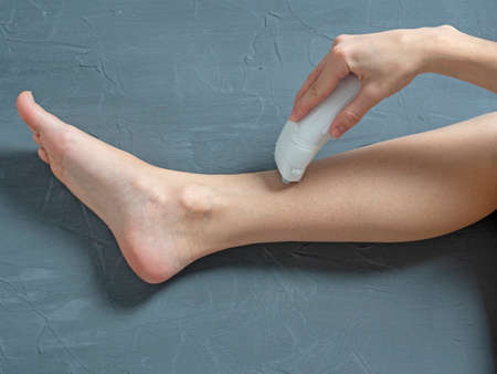 a woman shaves her leg with an electric epilator on a gray textured background. The concept of beauty and self-careの写真素材