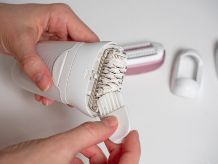 a woman holds and cleans an electric epilator with a brush on a white background. Maintenance of equipmentの写真素材