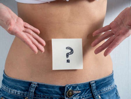 the woman points with her hands at a paper sticker with a question mark taped to her bare stomach. The concept of pregnancy and gender uncertaintyの写真素材