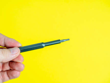 a man's hand holds a small screwdriver with a torx nozzle on a bright yellow background.の写真素材