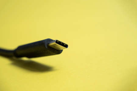 Black usb type C cable on yellow background. Copy space, a place for the text. Selective focus. Communication cable for connecting equipment and data transmissionの写真素材