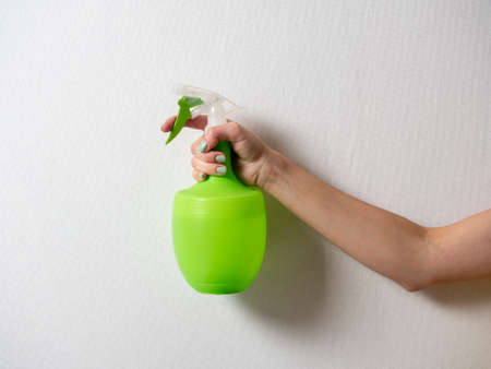 A woman's hand holds a plastic bottle with a green spray bottle on a gray background. The concept of home care and cleaning.の写真素材