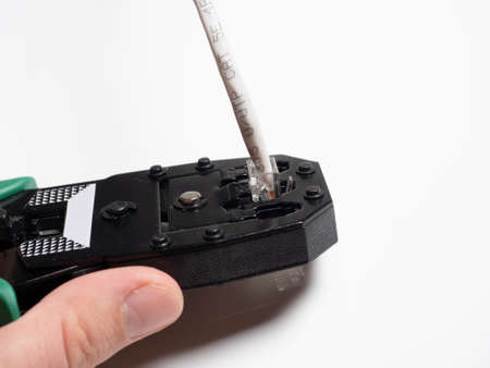 Swage for network telecommunication rj45 cables on a white surface. A cable is inserted into the...