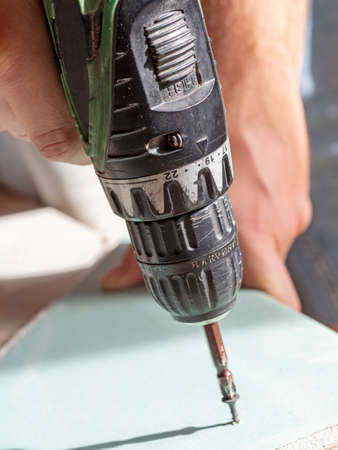 the man is holding a screwdriver and screwing the screw into the drywall from top to bottom. selective focusの写真素材