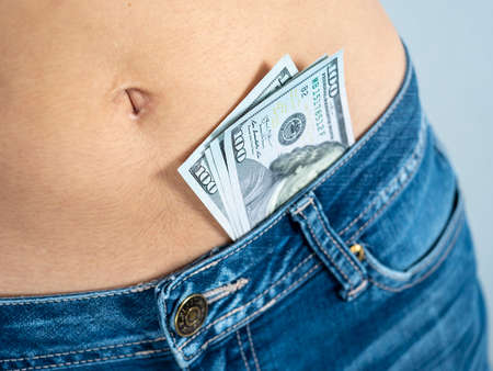 a woman in jeans with a bare stomach with dollars sticking out of her pants. The concept of...