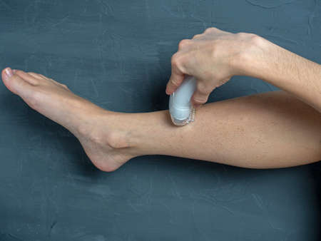a woman shaves her leg with an electric epilator on a gray textured background. The concept of...
