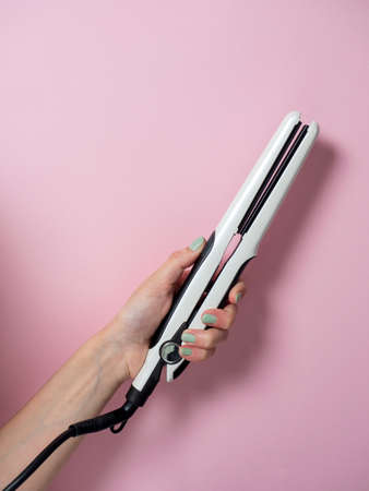 White curling iron in a woman's hand on a pnk background. An accessory for creating hairstyles. Beauty and fashion. Hair care.の写真素材