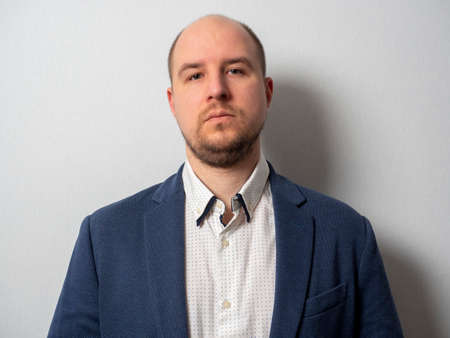 portrait of an adult man in a jacket and shirt, looking at the camera. Facial hair, bald head.