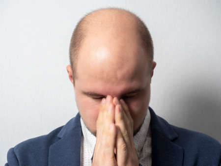 a large-scale portrait of a man in a suit who clutched the bridge of his nose with both hands and closed his eyes. Concept, fatigue, headache, migraine.の写真素材