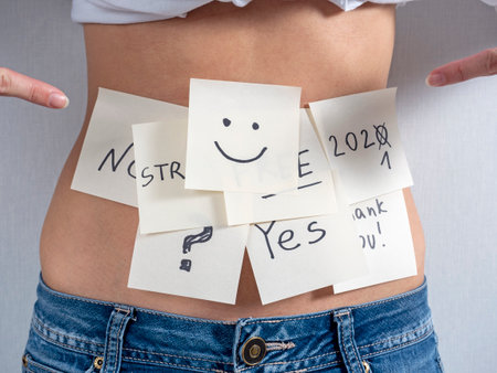a lot of paper stickers with different inscriptions and drawings are pasted on the bare stomach of a woman in jeansの写真素材