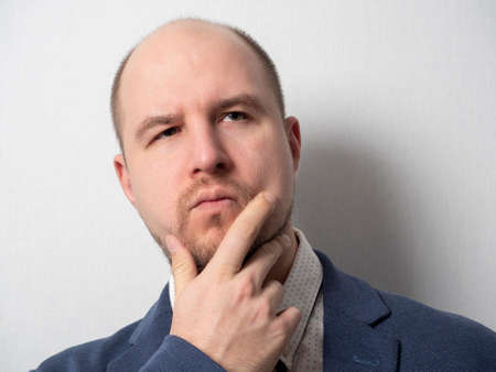 Portrait of a middle-aged man in a jacket and shirt, who looks thoughtfully to the side, Finger pressed to his cheek, beard, a little hair on his head, Caucasianの写真素材