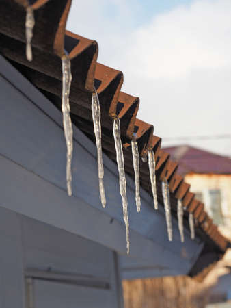Icicles hang on the roof. Close-up, selective focus, vertical photo