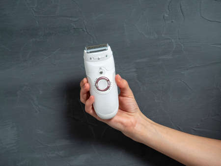Close-up of a female electric epilator in a female hand on a gray textured background.のeditorial素材