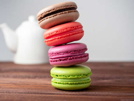 Delicious bright macaroons are stacked in a pyramid on a wooden background. In the background is a white teapotのeditorial素材