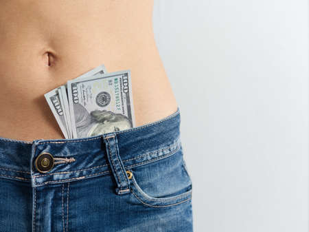 a woman in jeans with a bare stomach with dollars sticking out of her pants. The concept of...