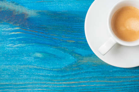 a white coffee mug with a full espresso is set on a saucer and on a blue wooden background. Coffee,...