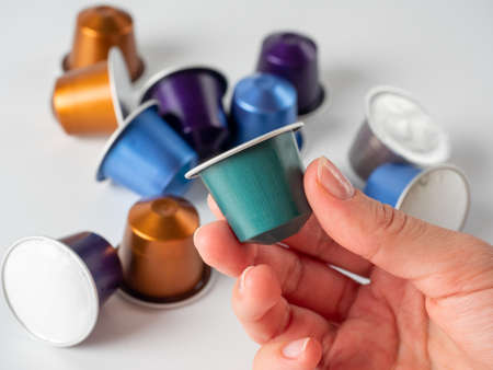 colored aluminum capsule with ground coffee in hand. White background with other capsules lying on it. Modern methods of making coffee. Capsule for coffee machineのeditorial素材