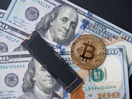 yellow bitcoin, an m2 SSD disk and hundred-dollar bills lie on a black background. The concept of...