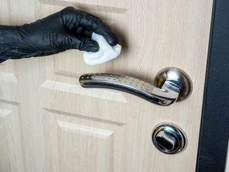 the hand of a man in a black latex glove wipes the handle of the front door with a rag. Disinfection of the interior from viruses and microbesの写真素材