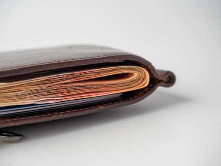 Close-up of a brown leather wallet full of banknotes on a white background. The concept of wealth,...