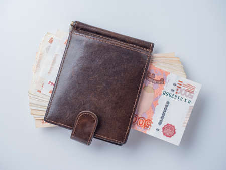 A close-up of a leather wallet full of 5000 rubles banknotes lies on a white background. Top view,...