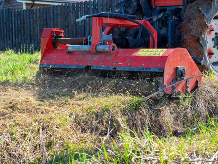 a tractor with a mower attached mulches dry grass along the fence. Land plot processingの写真素材