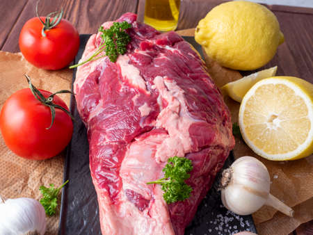 a piece of marbled beef lies on parchment surrounded by herbs, garlic, salt. Top view, flat lay....