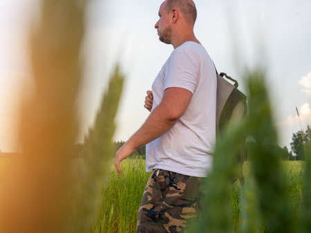 a man with a backpack goes into the field. Side view through the grass. The concept of vacation,...