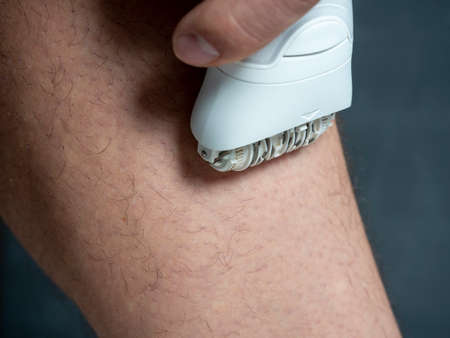 a man shaves his leg hair with a white electric depilator. Men's beauty. Close up