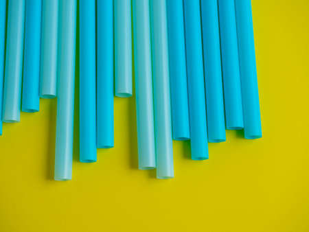 Close-up of plastic cocktail tubes of blue color on a yellow background. Top view, flat layの写真素材