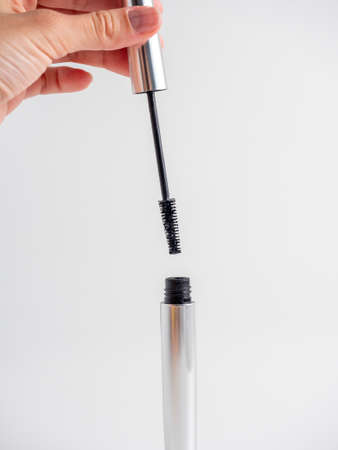 Women's hands hold the mascara open on a white background. A brush for applying mascara. The concept of cosmetics, vertical photoの写真素材