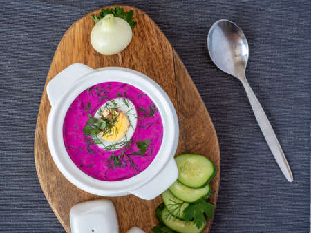Close-up of cold chlodnik soup on a wooden board. Soup of Polish Belarusian and Russian cuisine made of beetroot and kefir, decorated with half an egg. Healthy food. Top view, flat layの写真素材