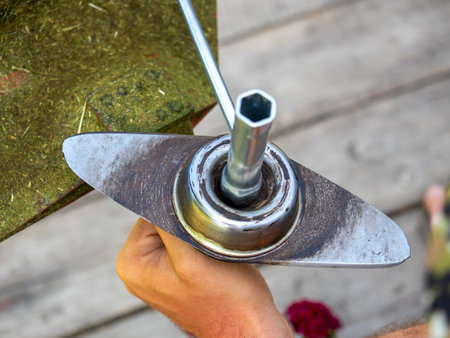 A man uses a key to unscrew the blade on the head of a gasoline trimmer. Close-up, a man at workの写真素材