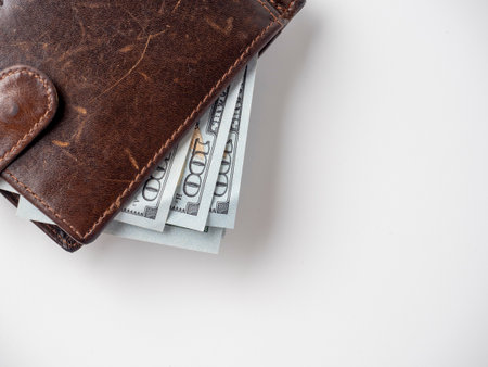 Close-up of a brown leather wallet stuffed with dollar bills on a white background. The concept of...