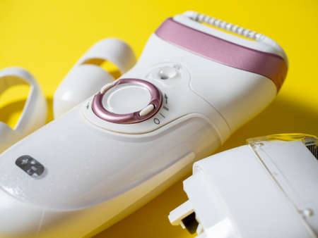 Close-up of the electric epilator for hair removal of white color on a yellow background. Next to the additional nozzle. Beauty products for maintaining beautyの写真素材