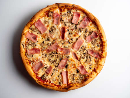 Close-up pizza with ham and mushrooms on a white background. A traditional Italian dish. A delicious and unhealthy dish. Top view, flat layの写真素材