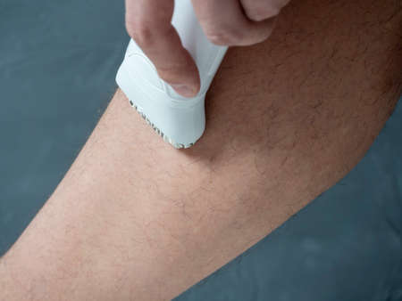 Close-up of a man removing hair from his leg using an electric depilator. Lots of leg hair. The...