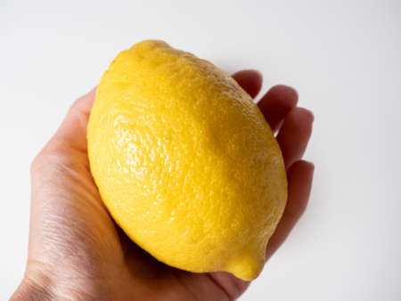 Close-up of a hand holding a yellow lemon. White background, side viewの写真素材