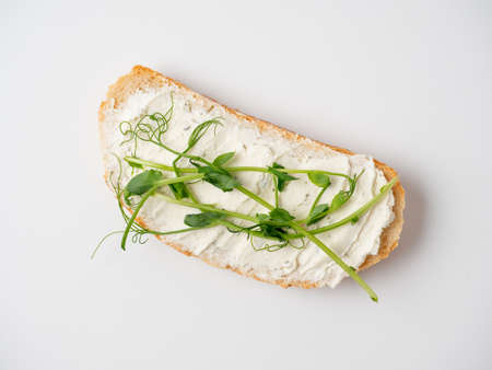 Close-up of a slice of bread spread with cottage cheese and decorated with micro greenery isolated...