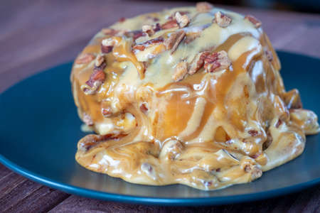 Sweet delicious dessert a cinnamon bun sprinkled with pecans and poured with caramel topping on a black plate and a turd background.の写真素材