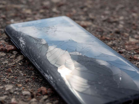 a broken phone on the asphalt in the sun. Cracks and broken glass, selective focusの写真素材