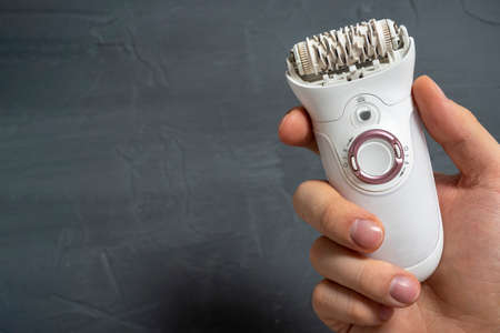 Close up Electric epilator in white color in a man's hand on a gray textured background. Means for hair removal, beauty care, beauty, copy space, place for text.の写真素材