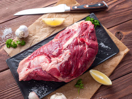 A piece of fresh raw beef lies on parchment surrounded by spices, herbs and vegetables. The knife is lying nearby. Top view, flat lay. Food compositionの写真素材